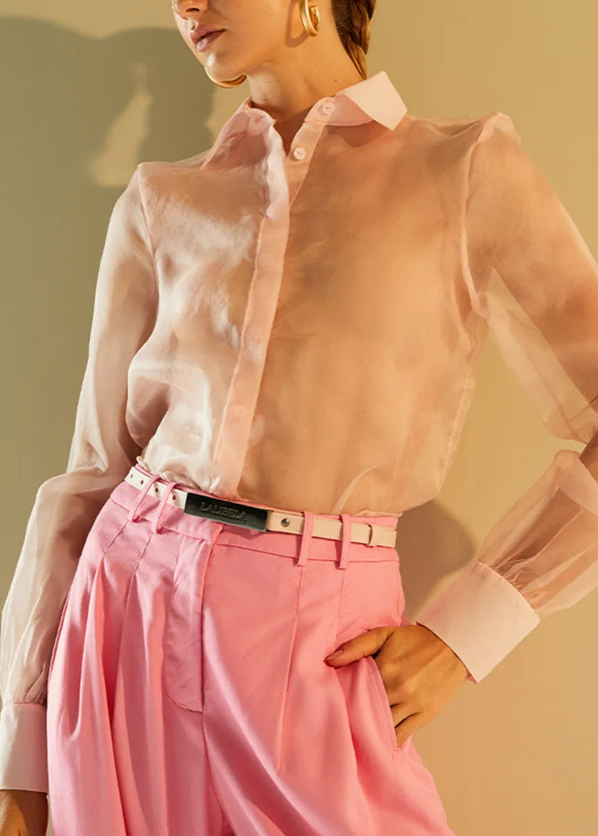 Person wearing a sheer pink blouse and pink pants against a beige background