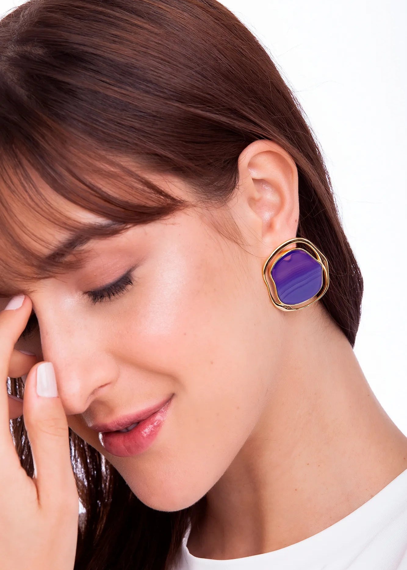 Woman wearing a gold earring with a purple gemstone on a white background