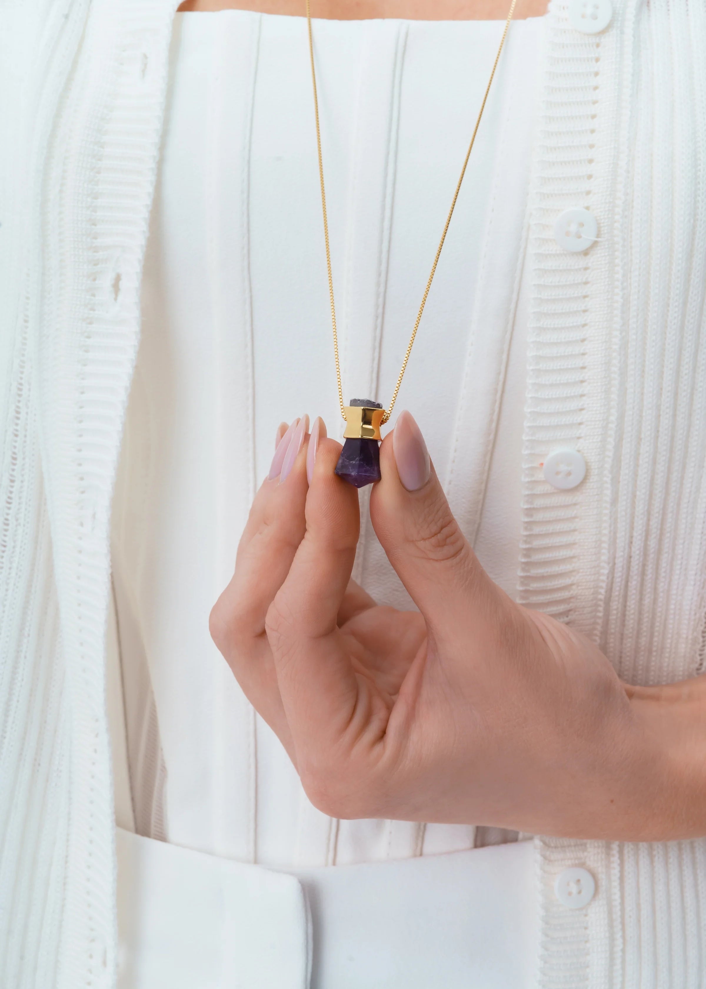 Hand holding a necklace with a purple pendant against a white background
