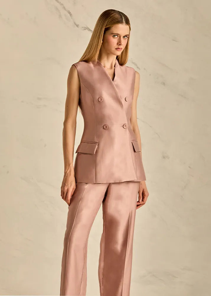 Woman wearing a pink sleeveless top and pants against a beige background