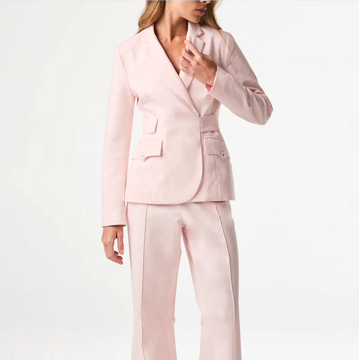 A woman wearing a light pink tailored blazer and matching wide-leg trousers against a clean white studio background.
