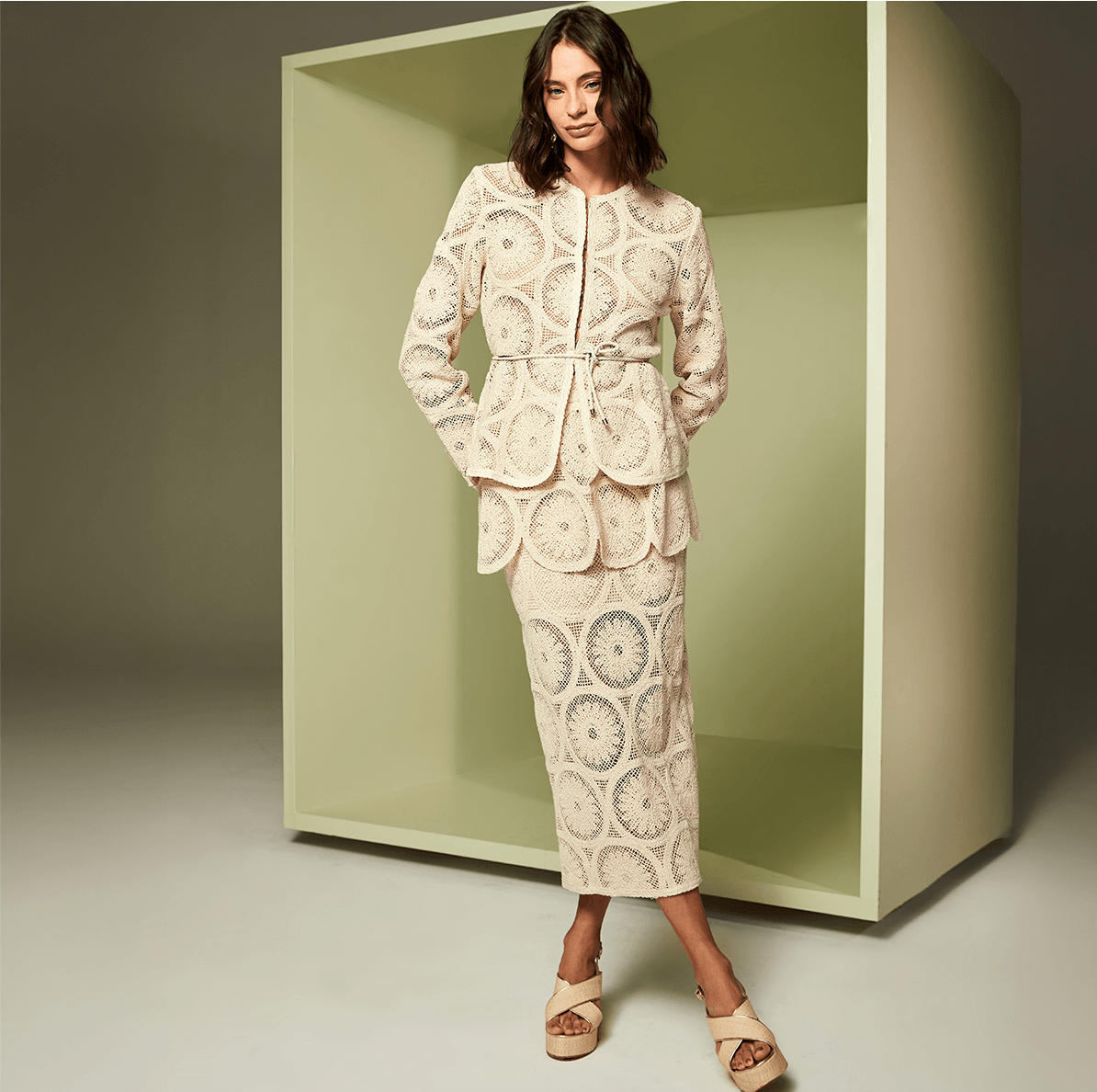 Woman wearing a beige lace outfit standing in front of a green box.