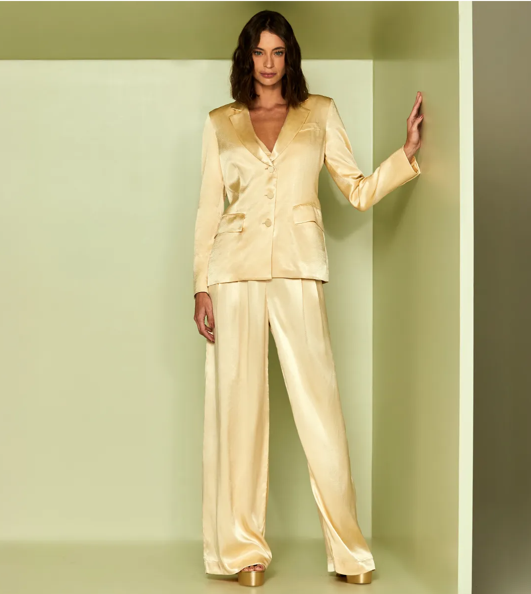 Woman wearing a gold satin suit against a plain background