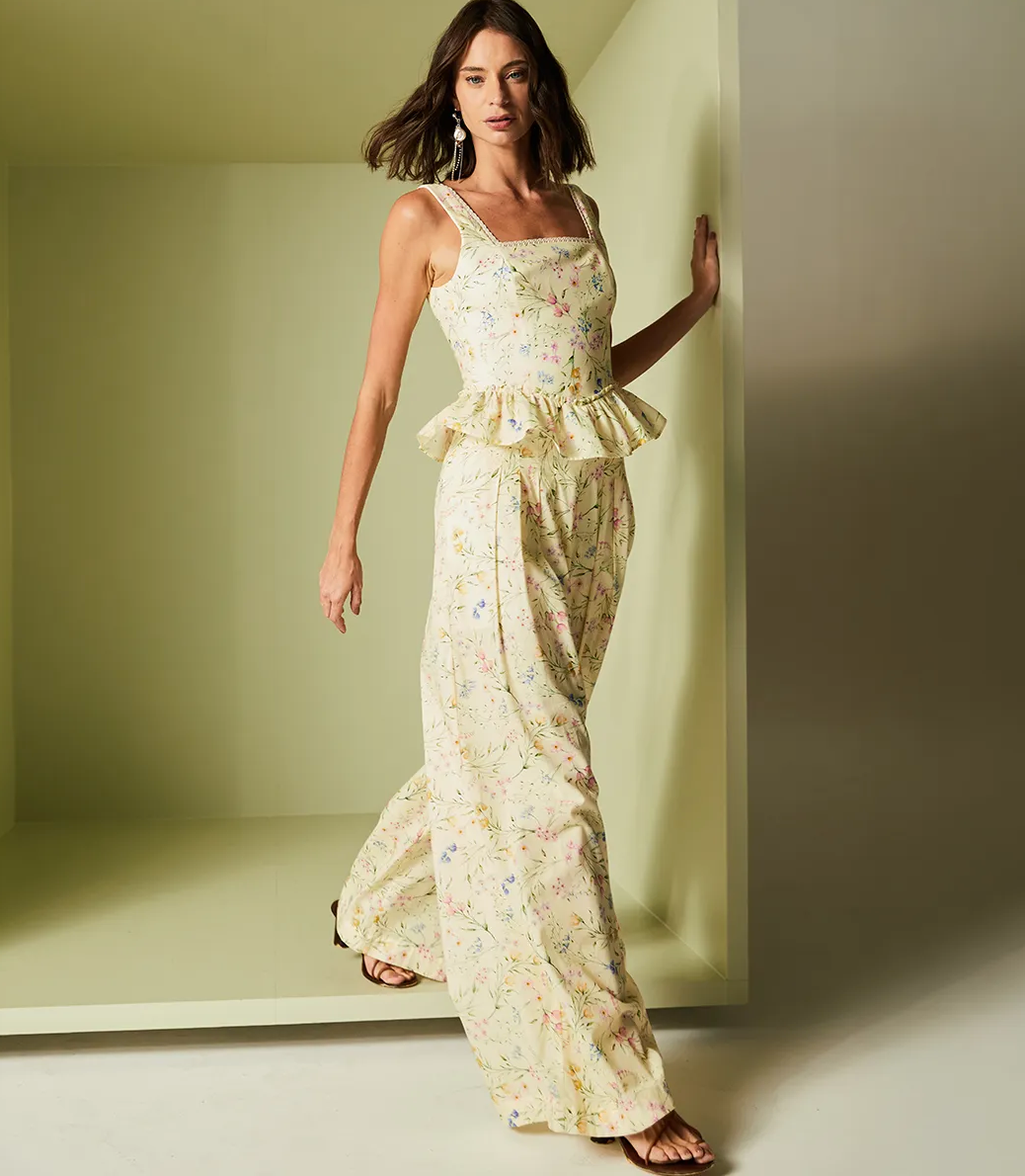 Woman wearing a floral dress standing against a plain wall.