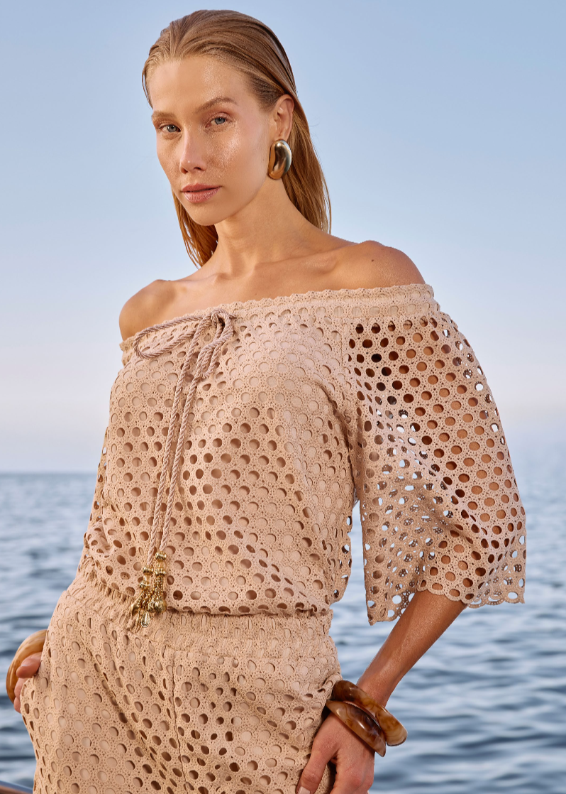 Woman wearing a beige crochet dress standing by the ocean.