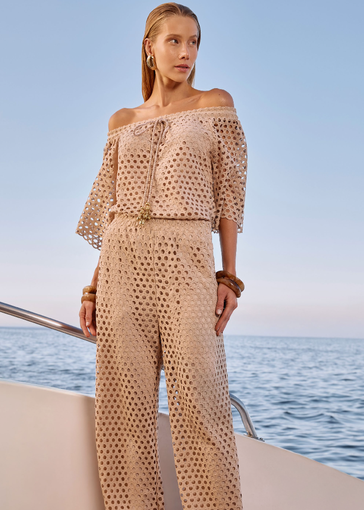 Woman in a beige patterned outfit standing on a boat with ocean and sky in the background