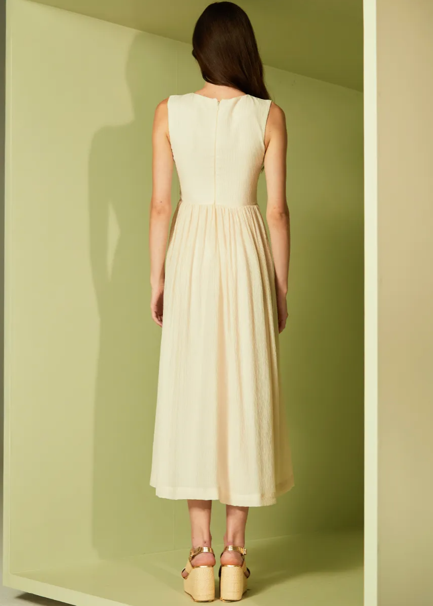 Woman wearing a beige dress standing in a minimalistic room with a neutral color scheme.