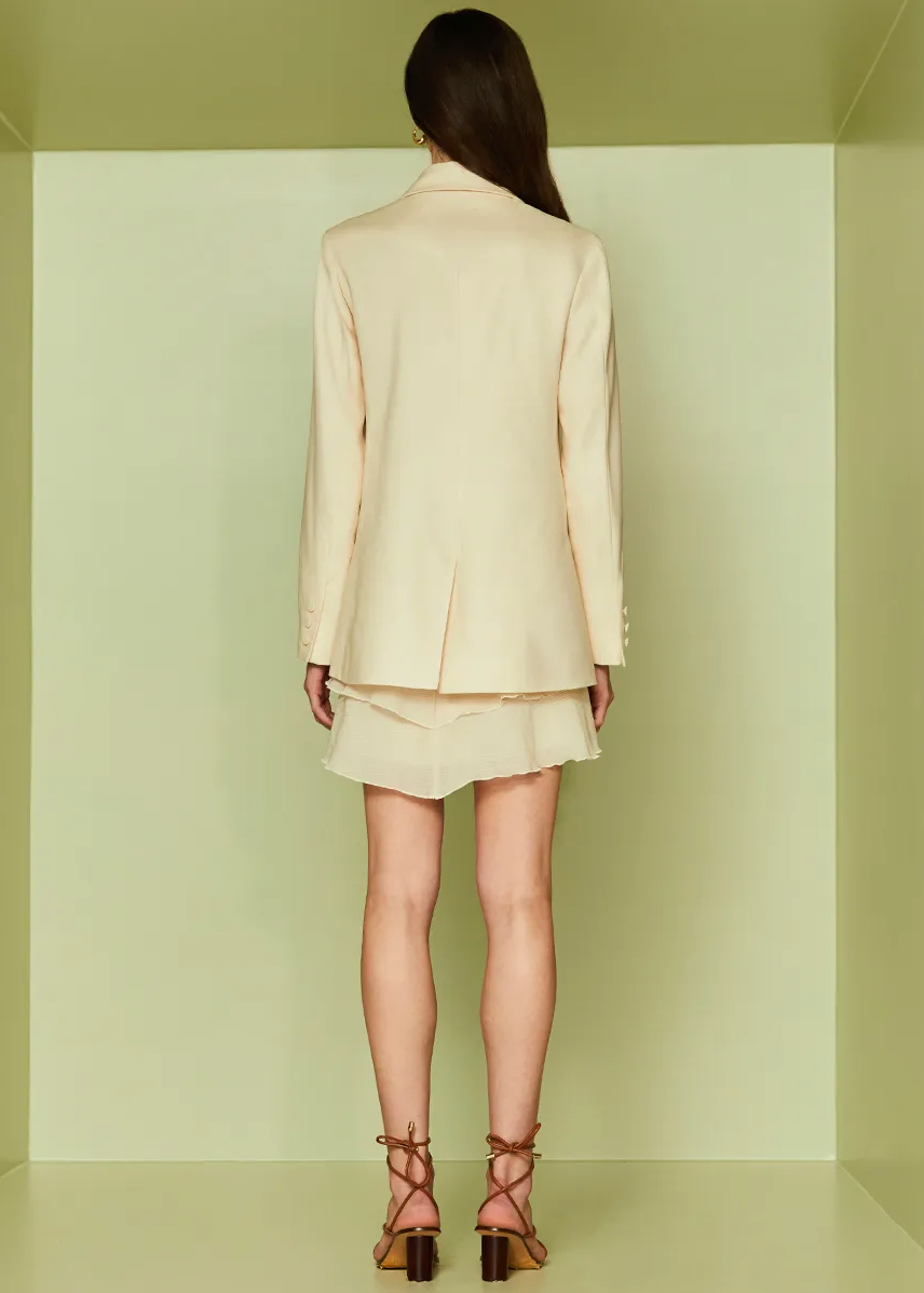Woman wearing a light-colored suit standing in a minimalistic room with green walls.