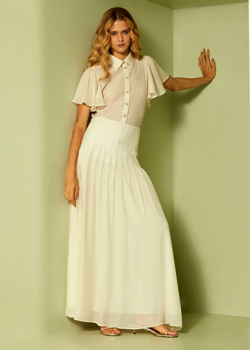 Woman wearing a light blouse and white skirt against a plain background