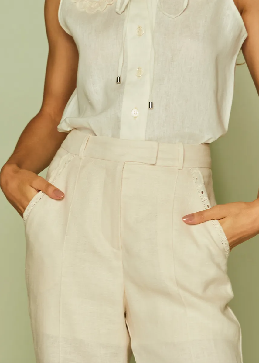 Person wearing a white sleeveless top and beige pants against a light green background