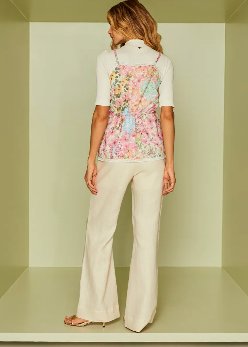 Woman wearing a floral top and white pants standing inside a light green box.