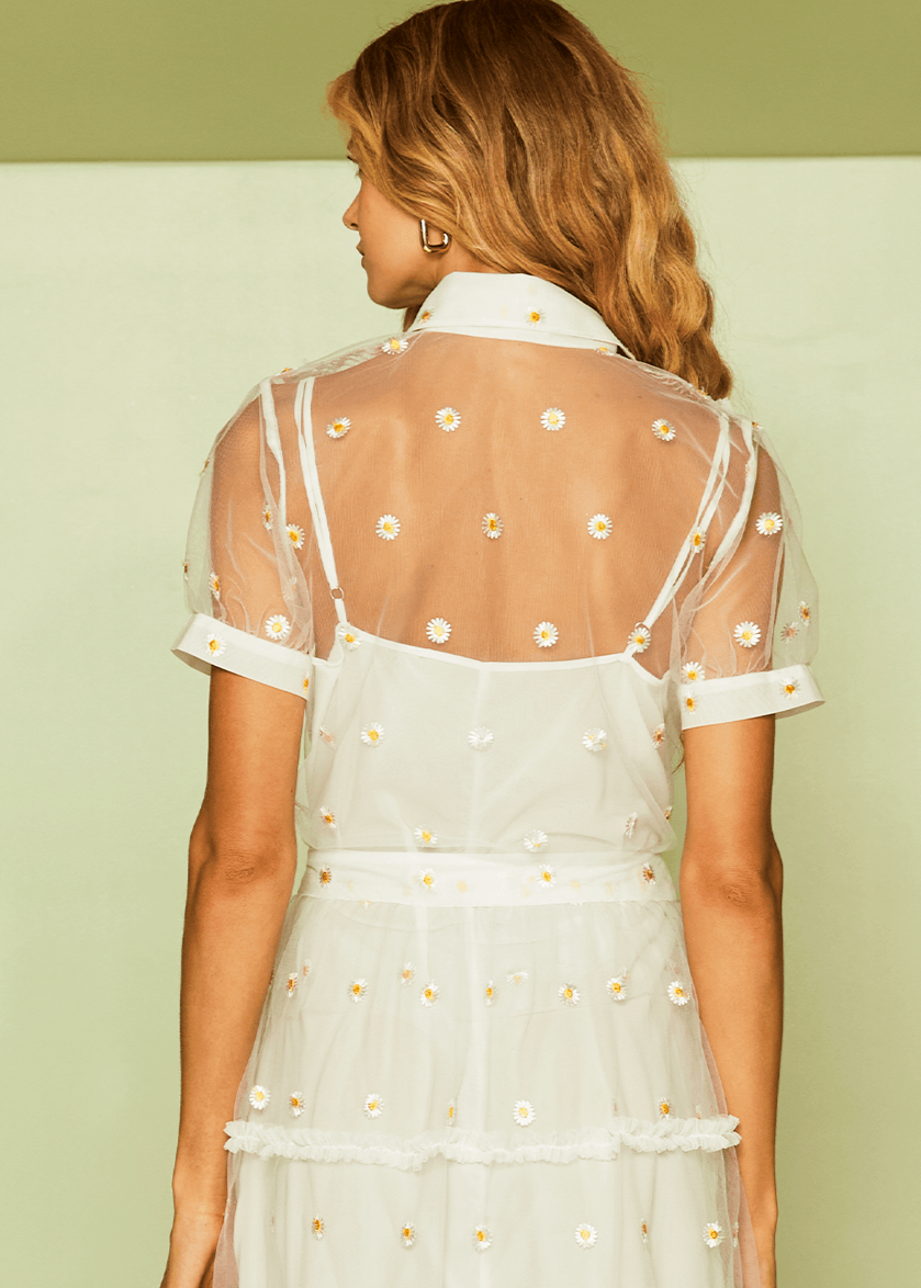 Woman wearing a white dress with sheer sleeves and floral details on a light green background