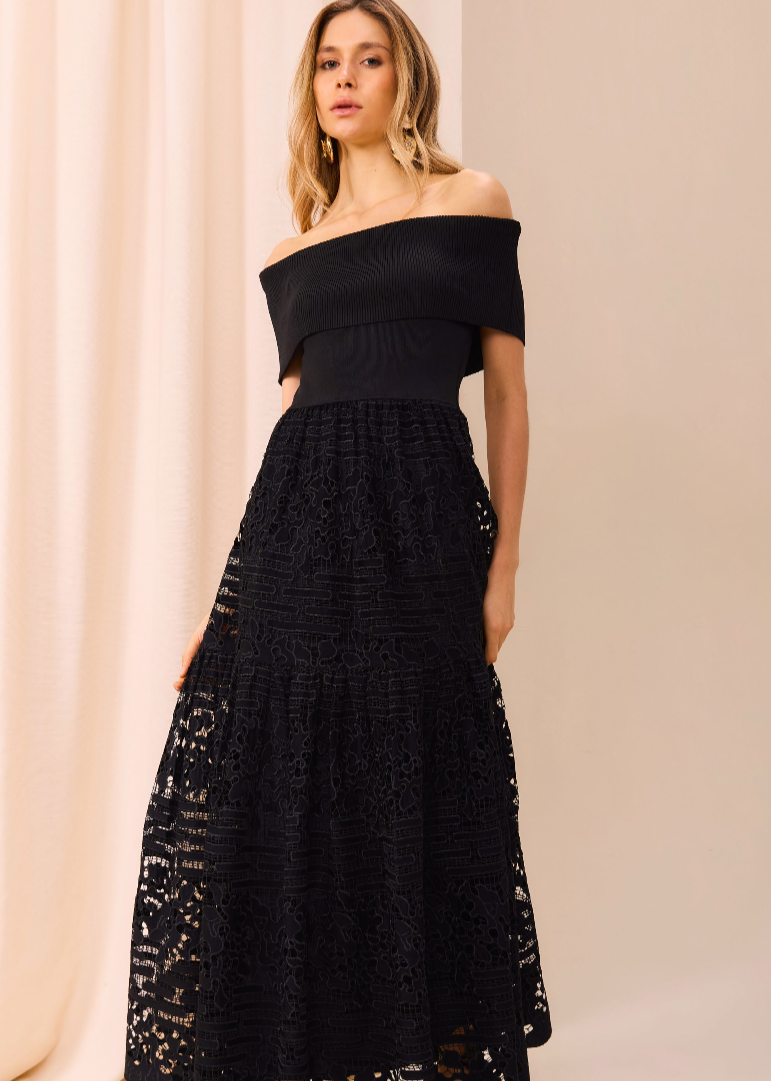 Woman wearing a black off-shoulder lace dress against a beige curtain background