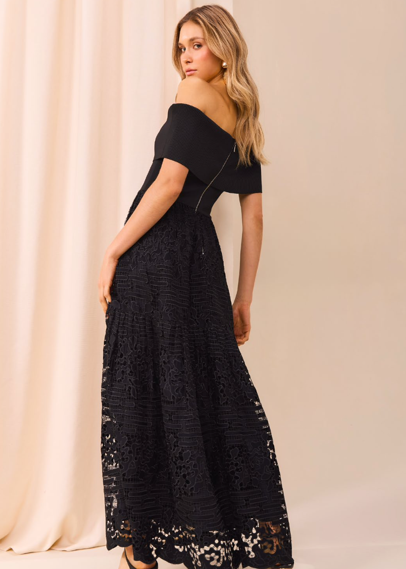 Woman wearing a black lace dress against a beige curtain background