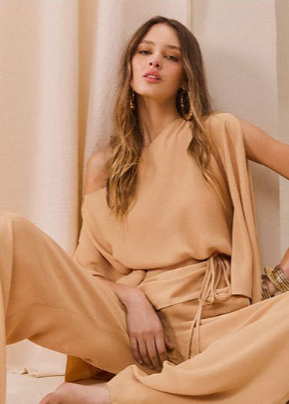 Woman in a beige outfit sitting against a beige curtain