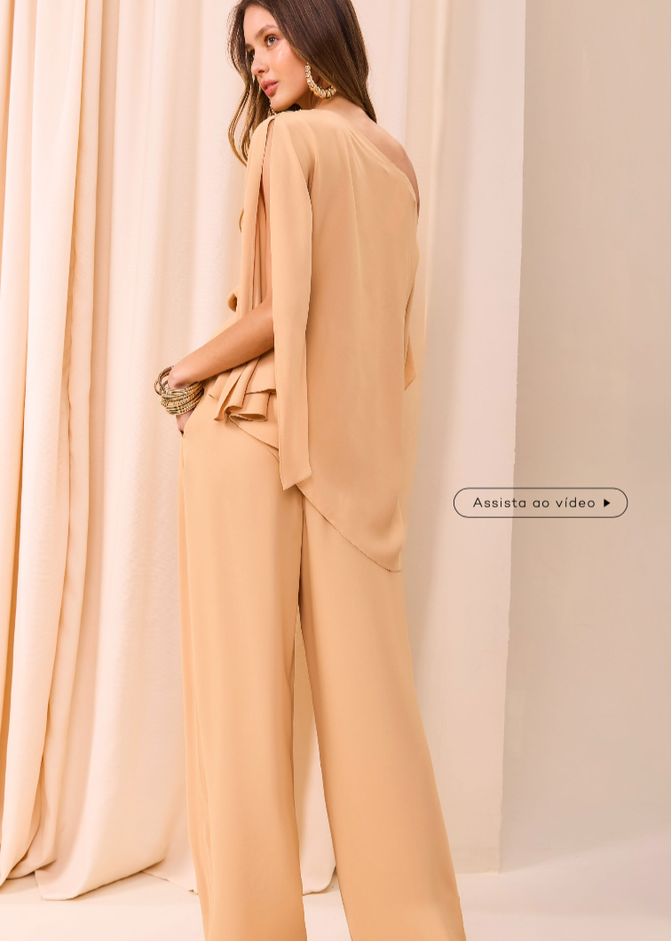 Woman wearing a beige suit standing in front of a curtain.