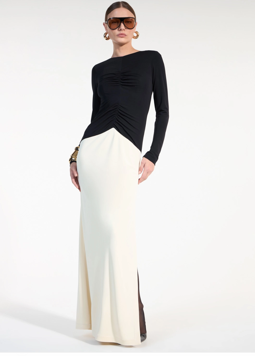 Woman wearing a black long-sleeve top and white maxi skirt on a white background