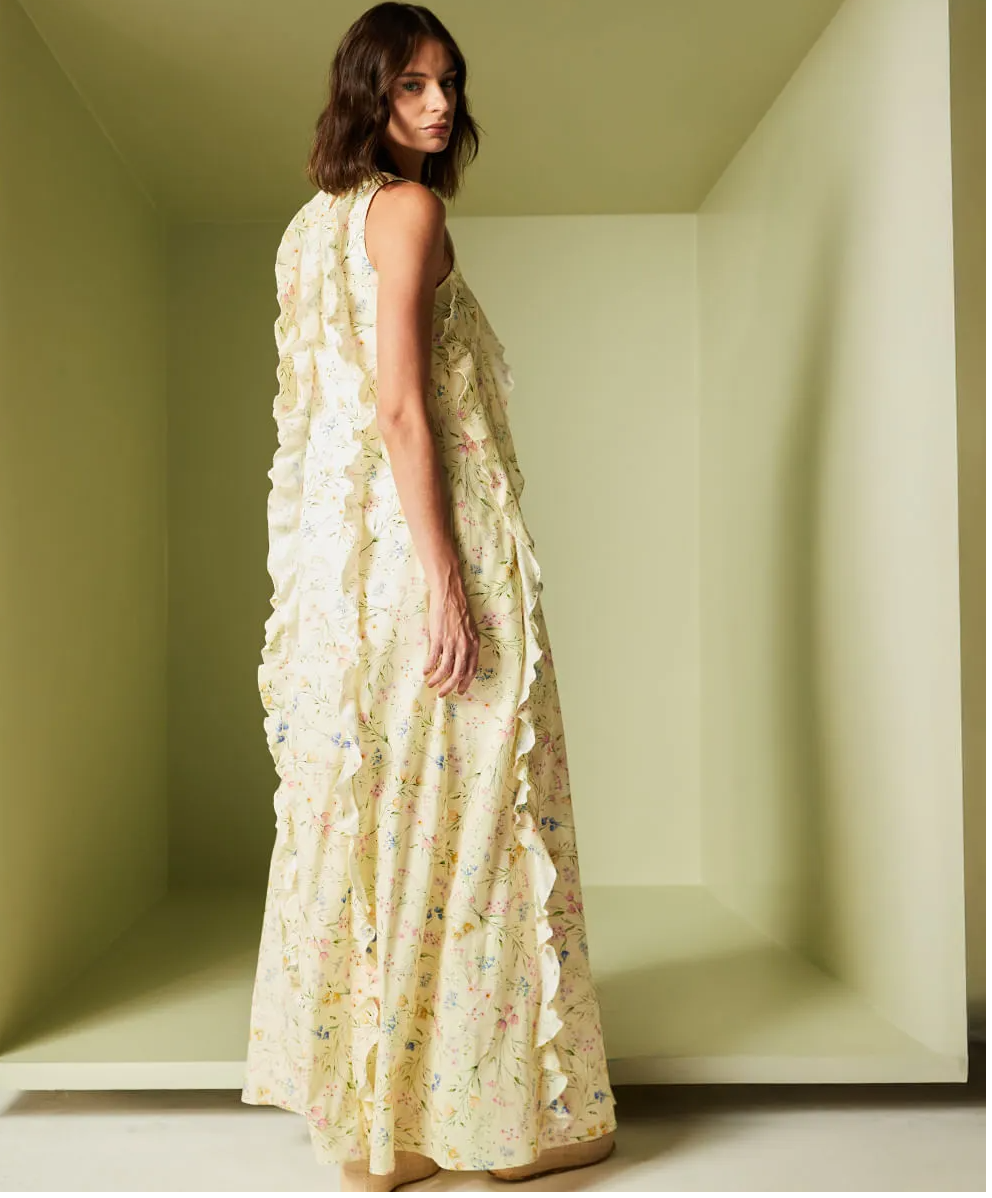 Woman wearing a long, light-colored floral dress in a minimalistic room.
