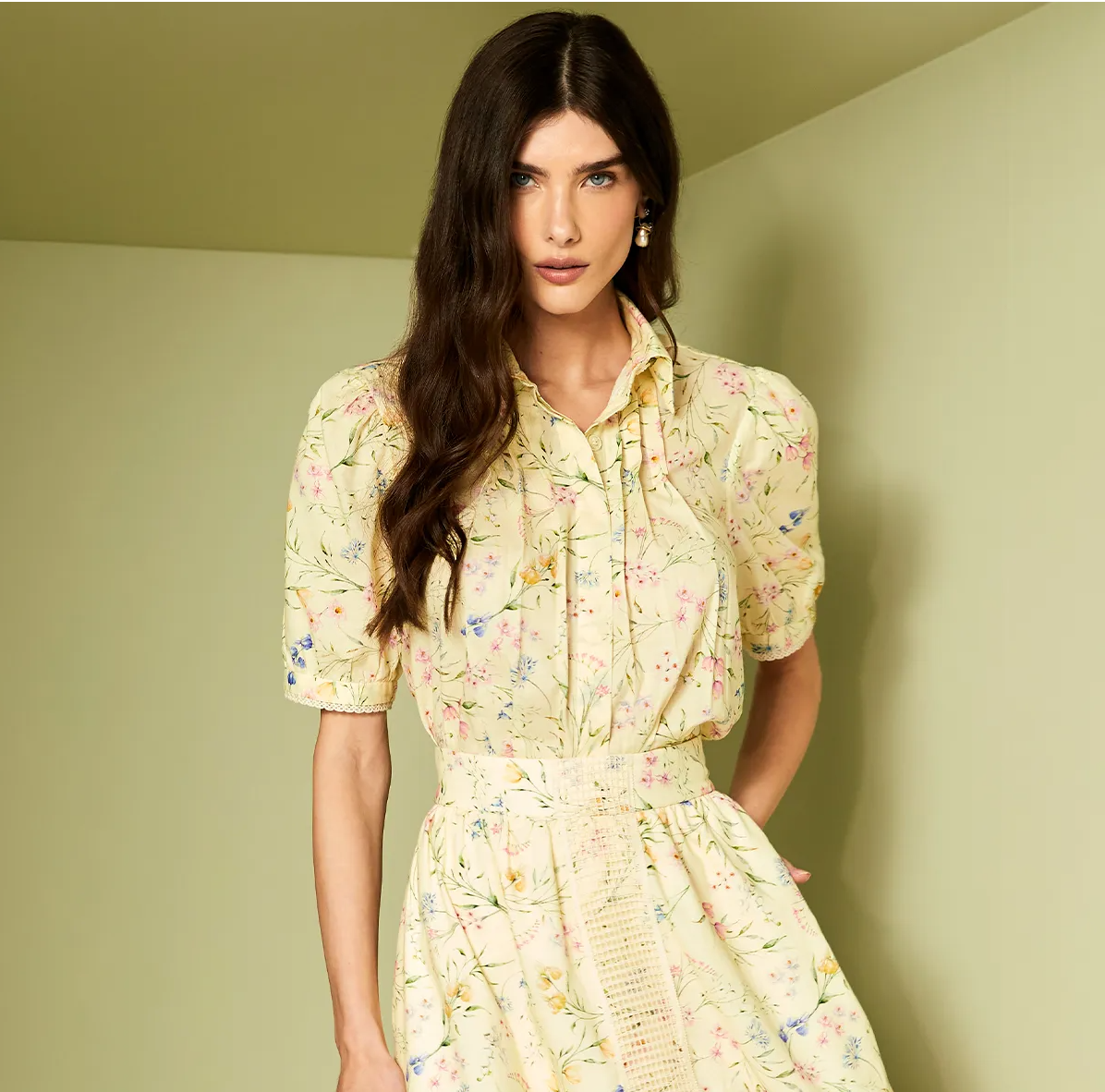 Woman wearing a yellow floral dress against a light green wall