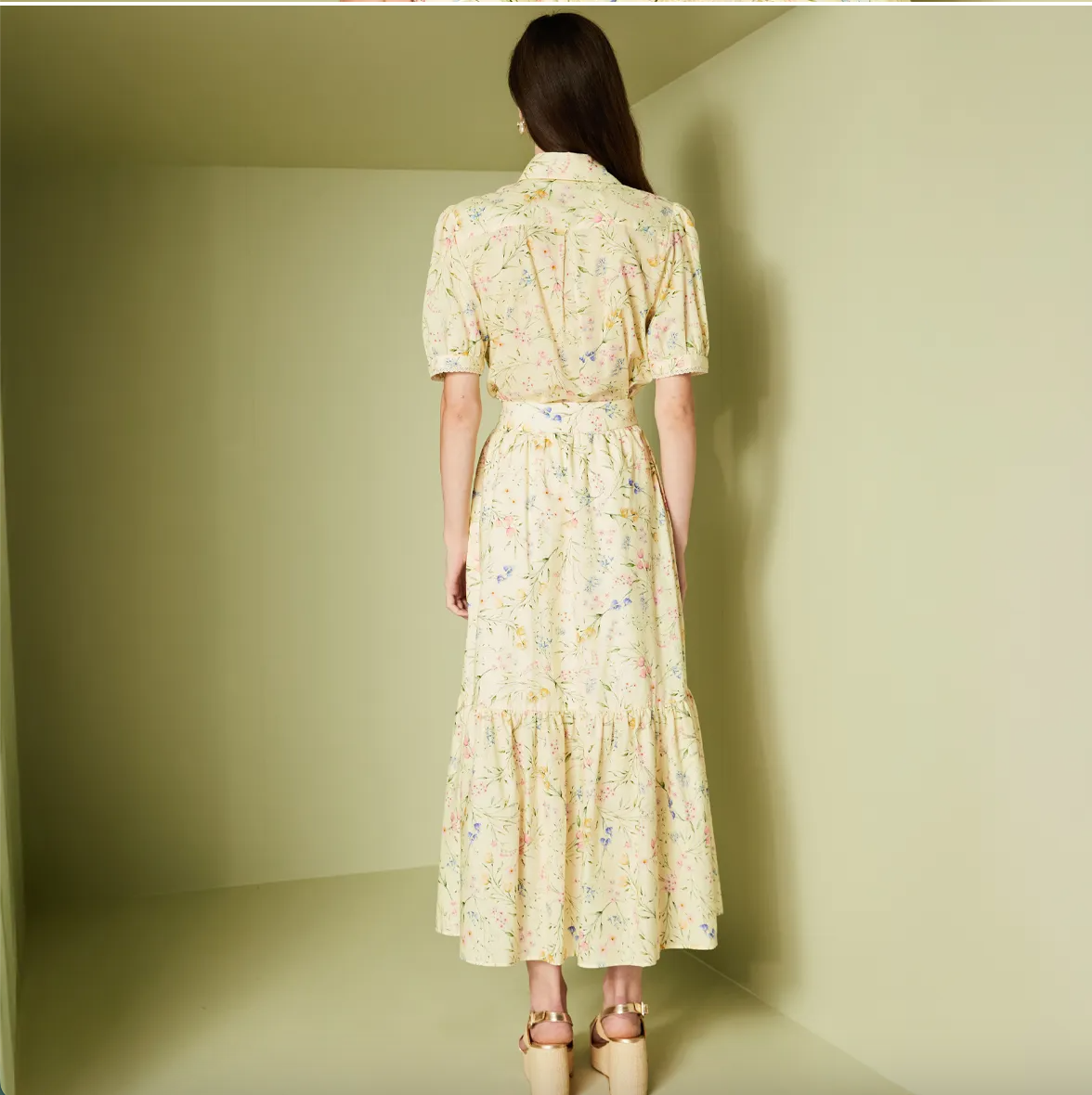 Woman wearing a floral dress standing against a plain wall