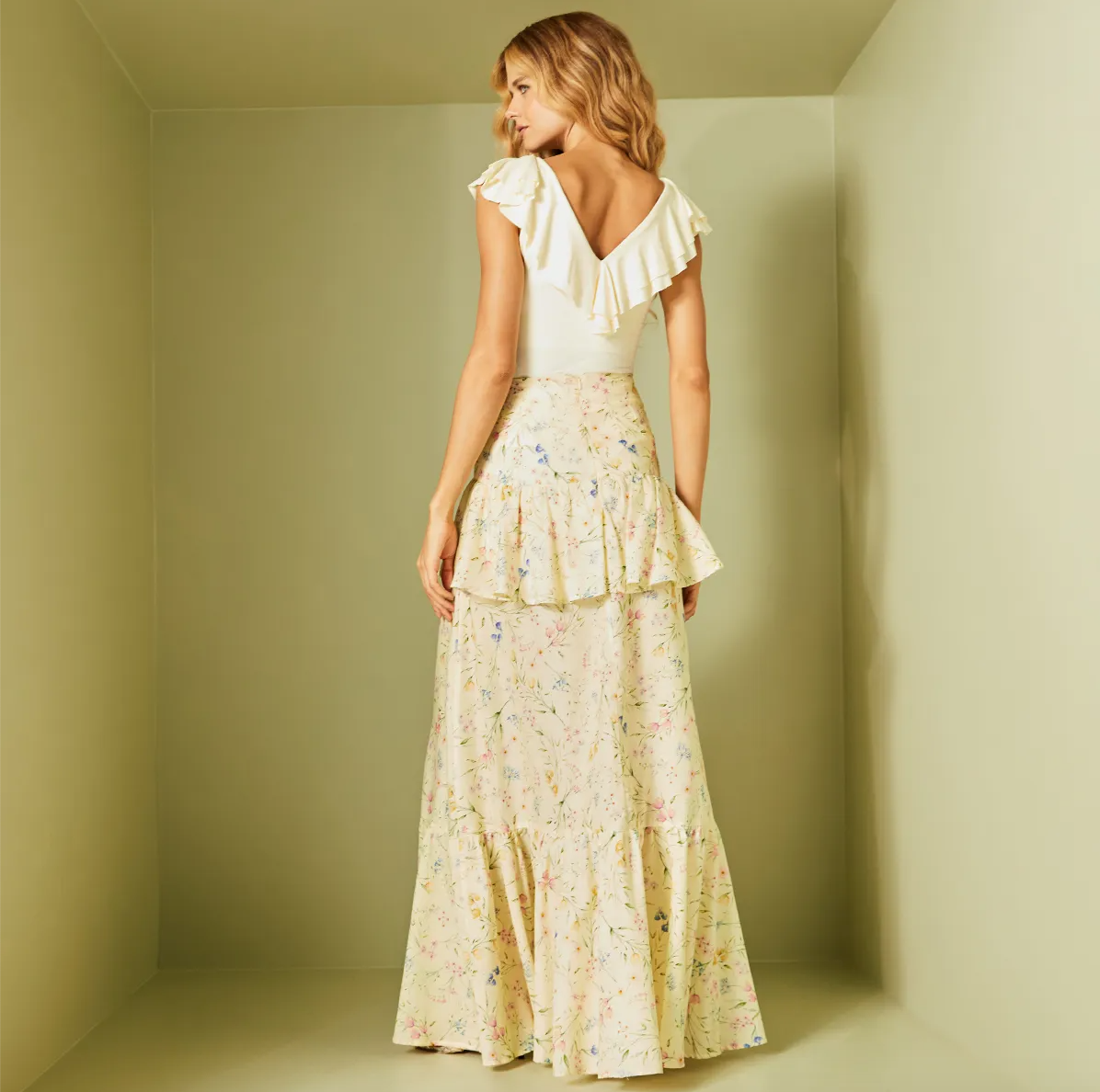 Woman wearing a white top and floral skirt in a minimalistic setting