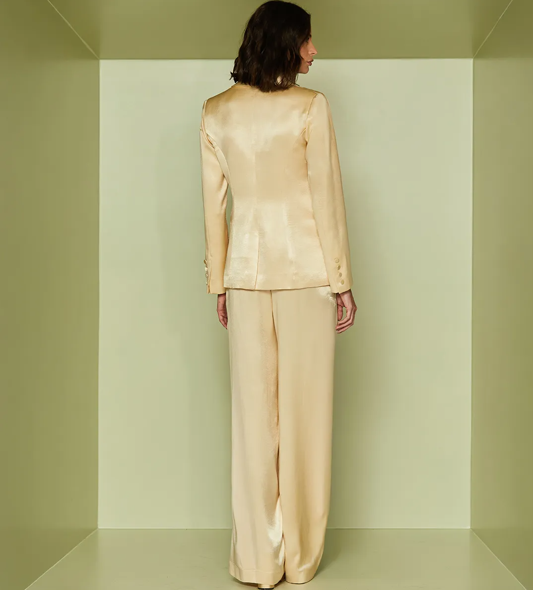 Woman wearing a beige suit standing in a minimalistic room with green walls.