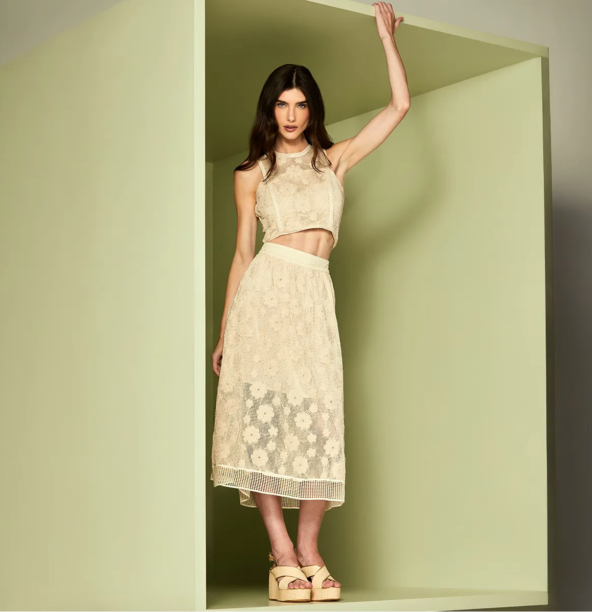Woman wearing a beige lace dress standing in a green box.