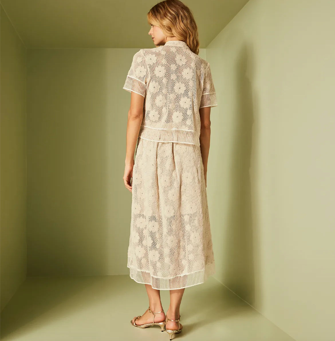 Woman wearing a light-colored lace dress standing in a minimalistic room.