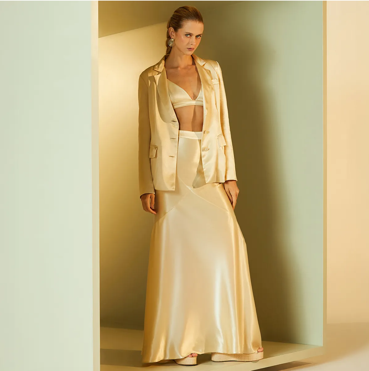 Woman wearing a beige satin suit standing against a neutral wall.