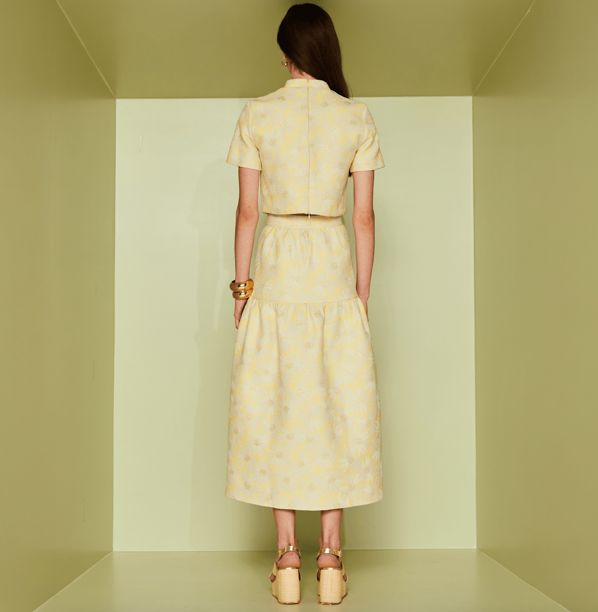Woman wearing a yellow patterned dress standing in a minimalistic room.