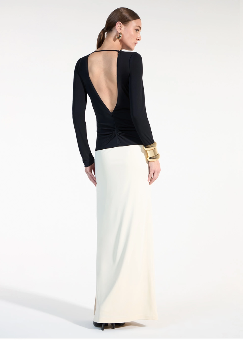 Woman wearing a black long-sleeve top with a deep neckline and a white skirt on a white background