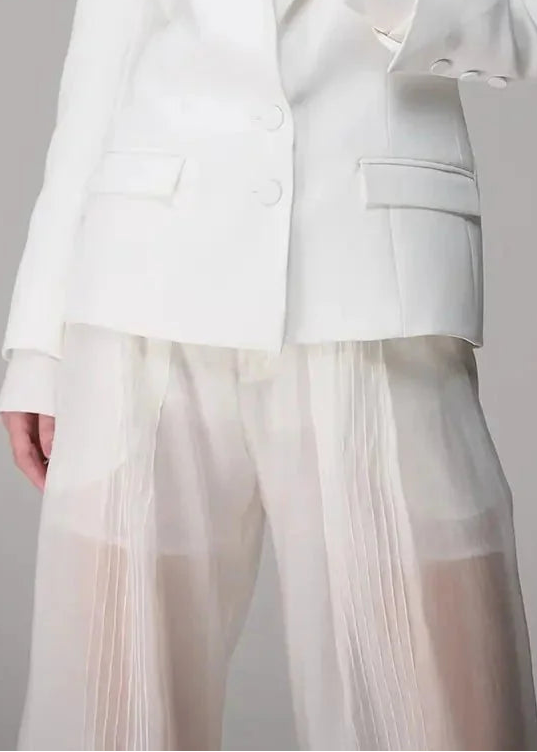 Woman wearing a white suit with sheer pants against a gray background
