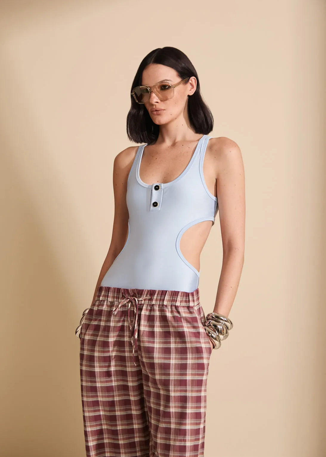 Woman wearing a light blue bodysuit with cut-out design and plaid pants on a beige background