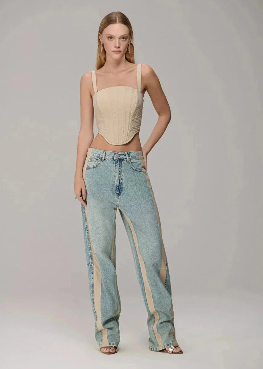 Woman wearing a beige top and blue jeans with beige stripes on a gray background