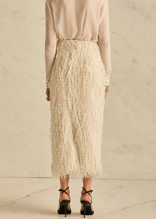 Woman wearing a light-colored blouse and fringed skirt against a neutral background