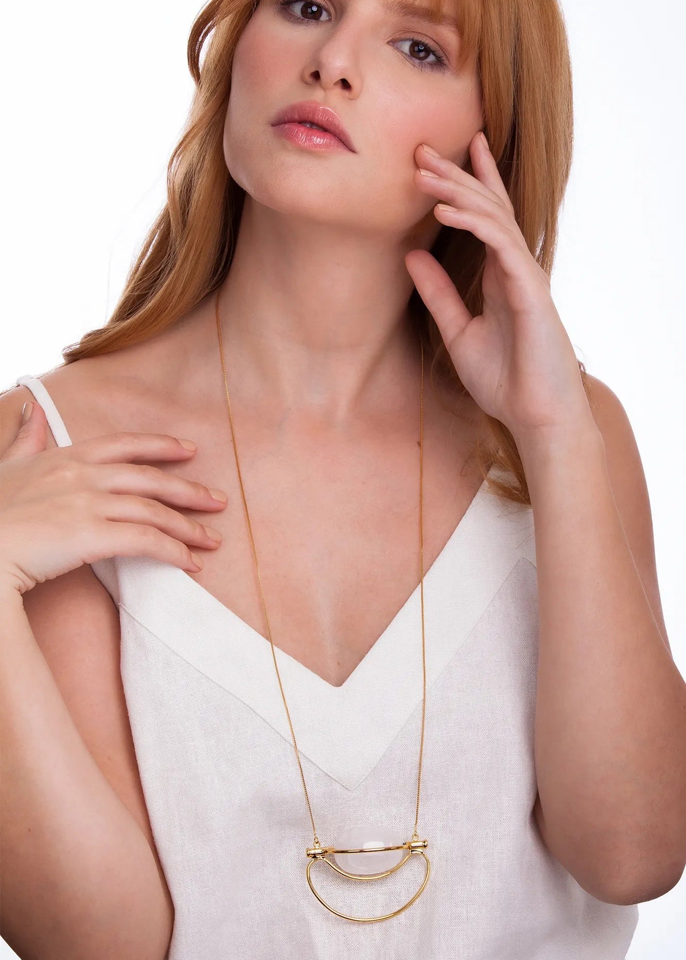 A woman wearing a delicate gold necklace with a double crescent moon pendant, styled with a white V-neck top against a clean white background.