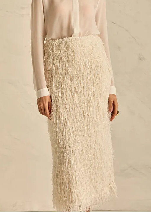 Woman wearing a light blouse and white lace skirt against a neutral background