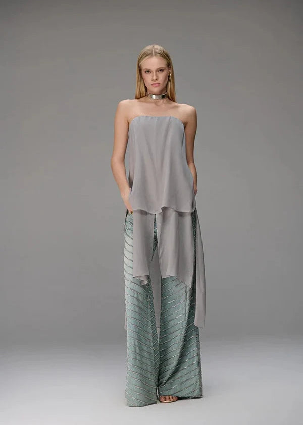 Woman wearing a strapless top and wide-leg pants on a gray background