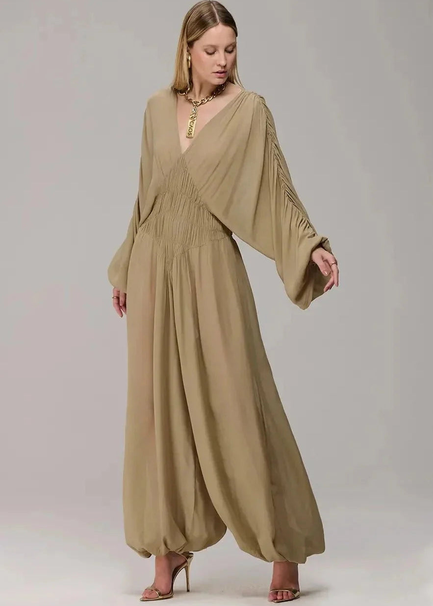 Woman wearing a long beige dress with wide sleeves on a plain background