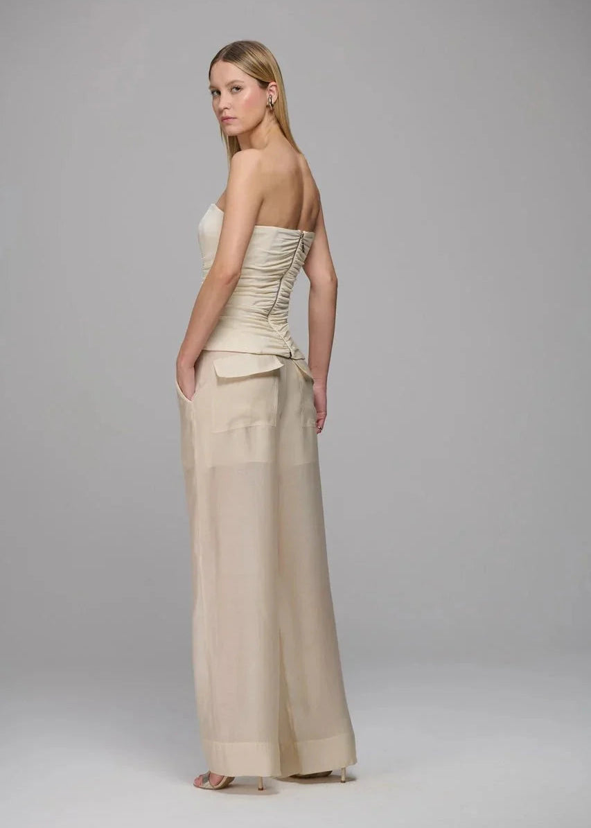 Woman wearing a beige strapless top and wide-leg pants on a gray background