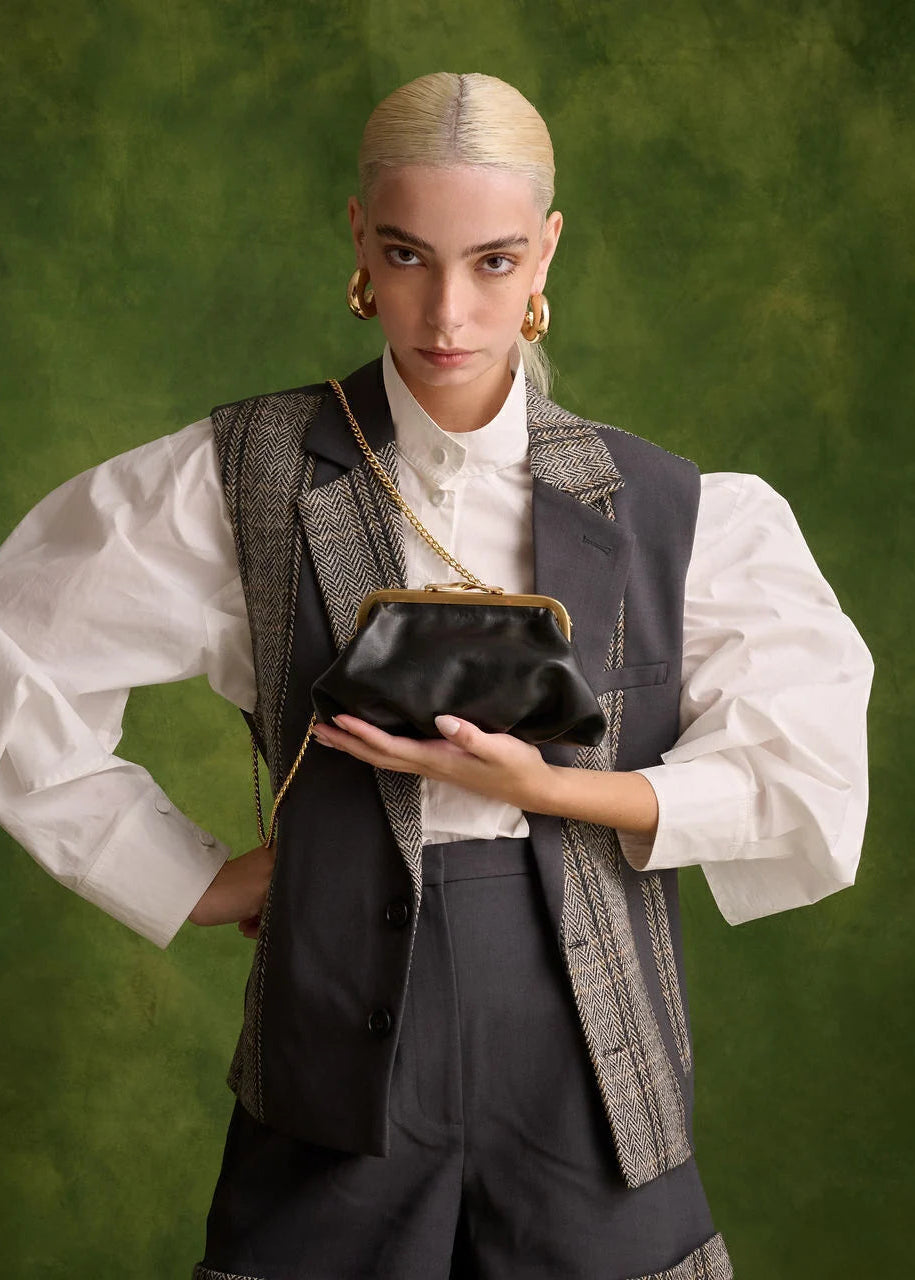 Person holding a black handbag against a green background