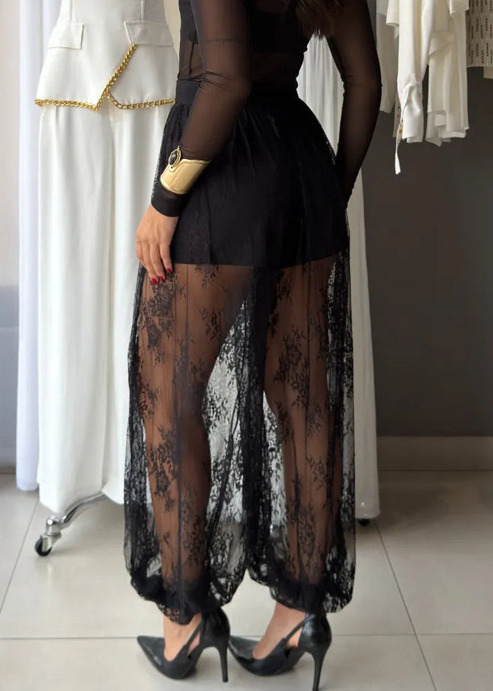 Woman in a black outfit standing in a clothing store with mannequins and racks of clothes.