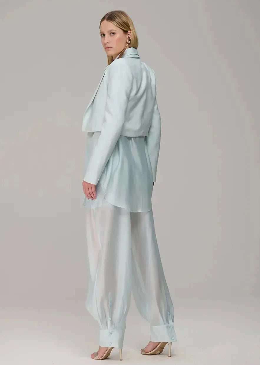 Woman wearing a light blue outfit with a jacket and pants on a plain background