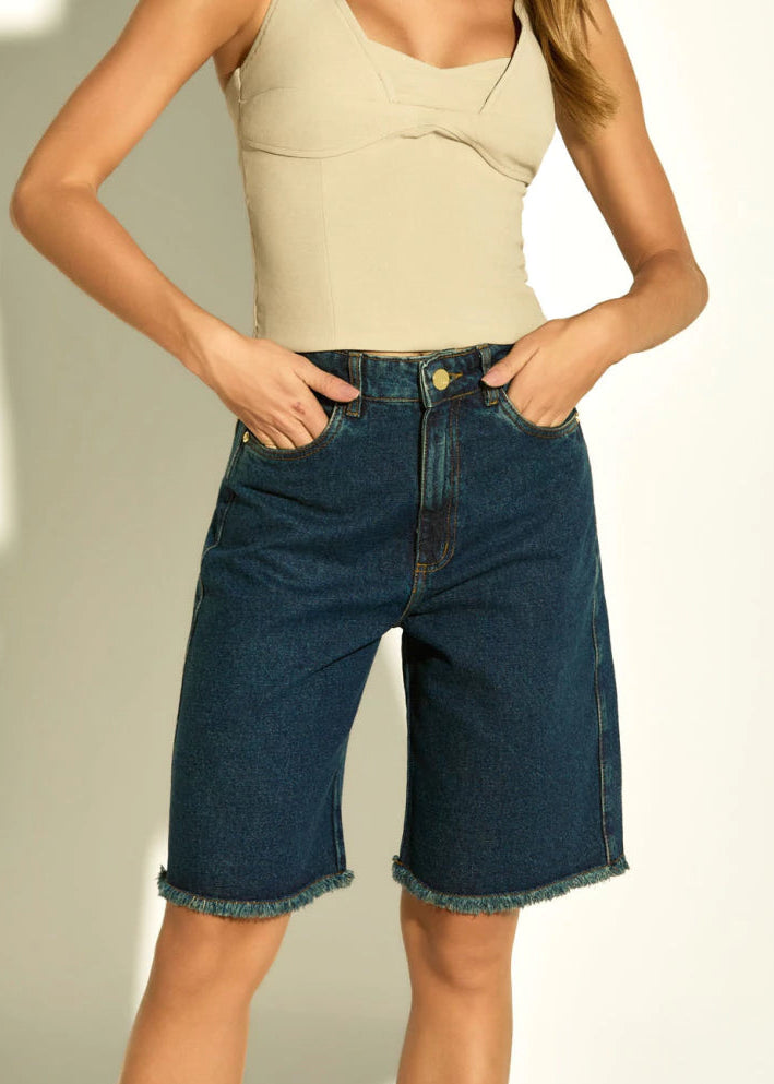 Woman wearing a beige top and blue denim shorts against a white background