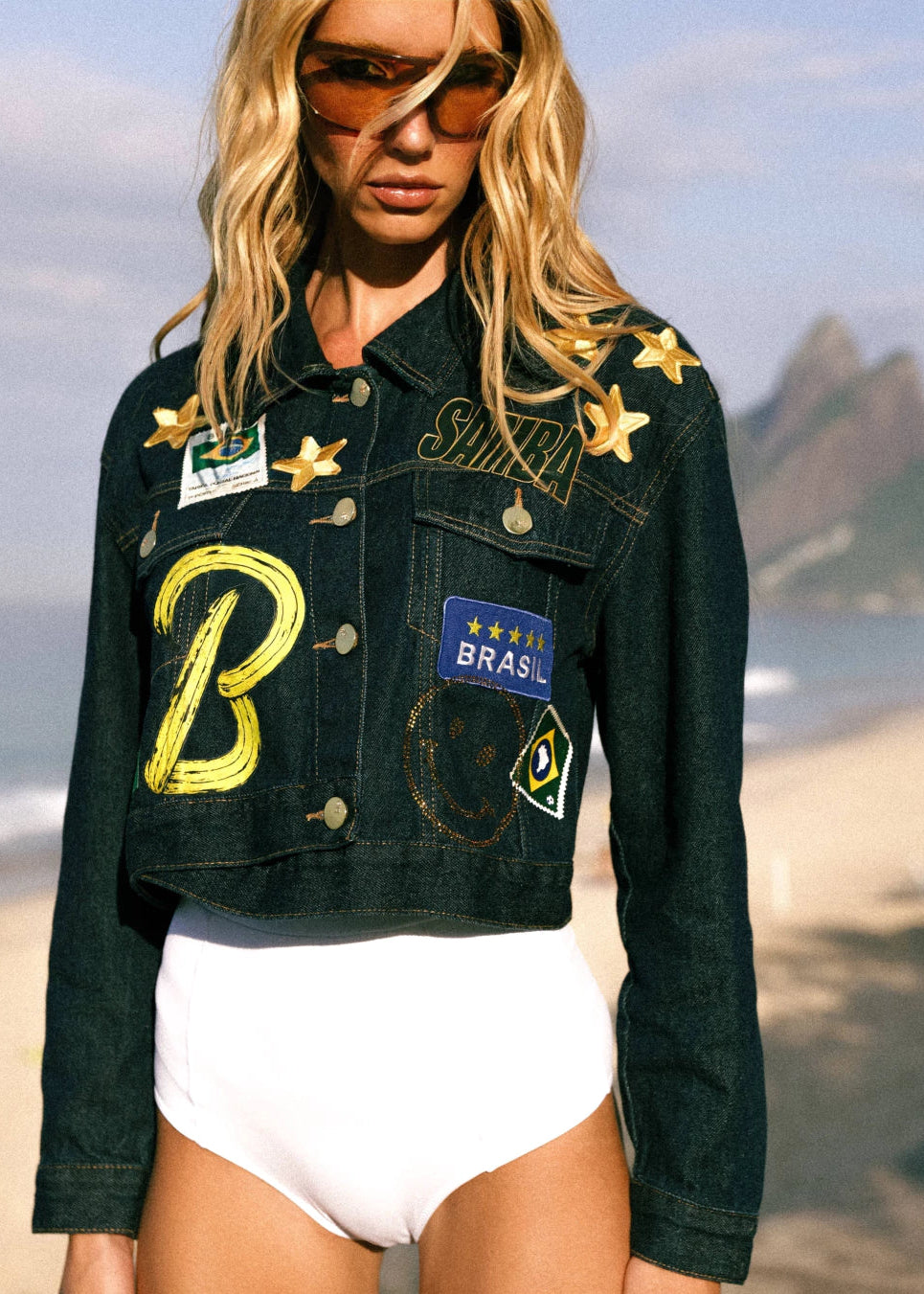 Woman wearing a black denim jacket with patches on a beach