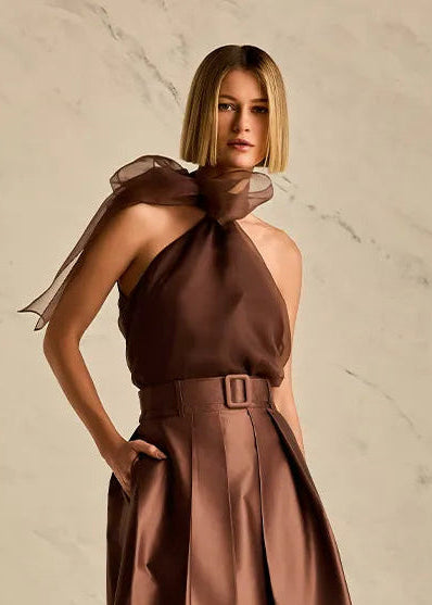 Woman wearing a brown blouse with a belt against a beige background