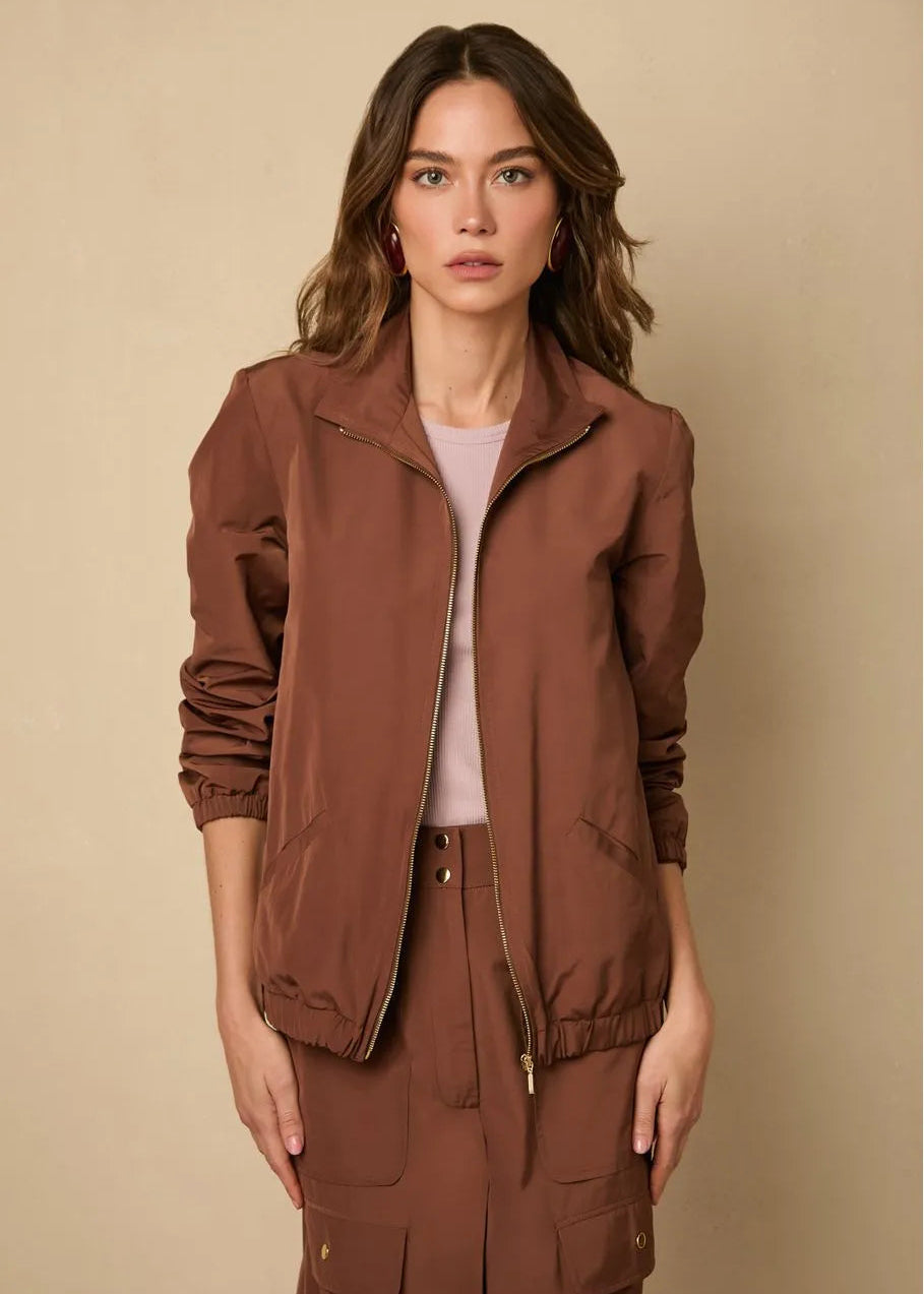 Woman wearing a brown jacket and pants against a beige background