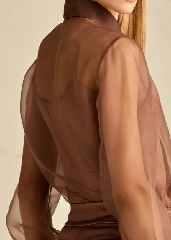 Woman wearing a sheer brown blouse against a neutral background