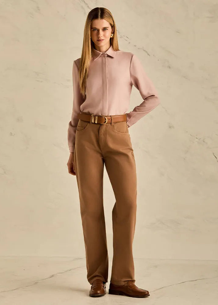 Woman wearing a pink blouse and brown pants against a beige background