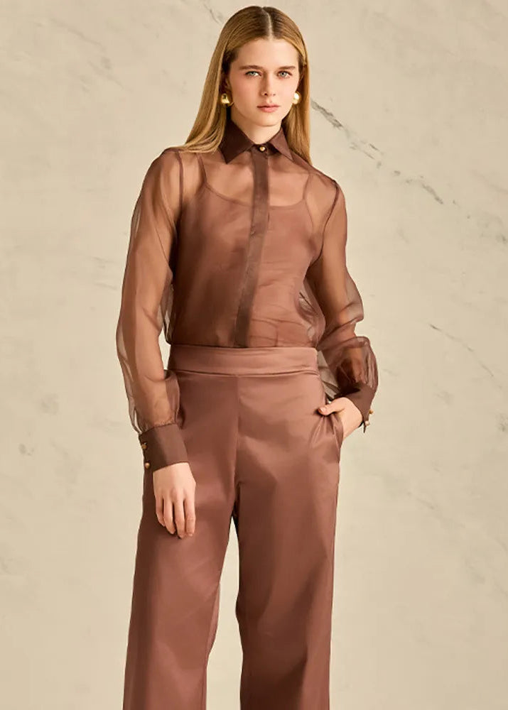Woman wearing a brown outfit with sheer sleeves against a beige background